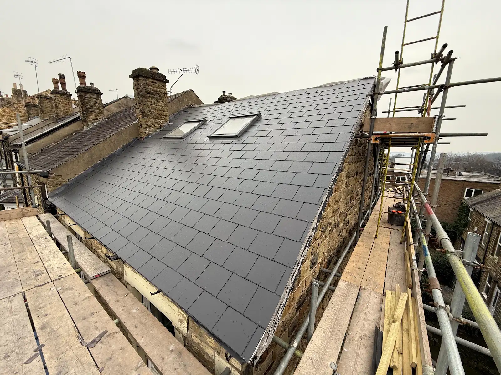 New slate roof with two rooflight windows beside access scaffolding