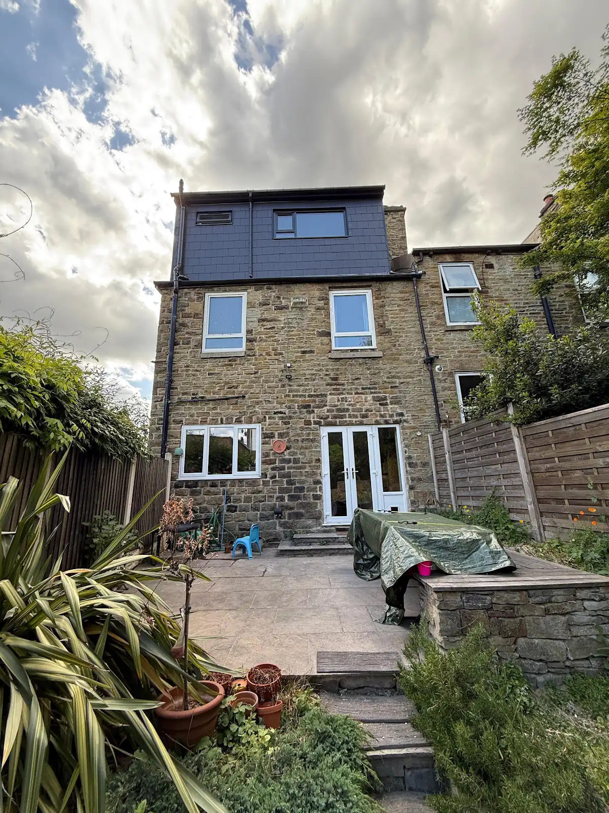 Rear dormer with dark slate cladding and two windows above a stone house